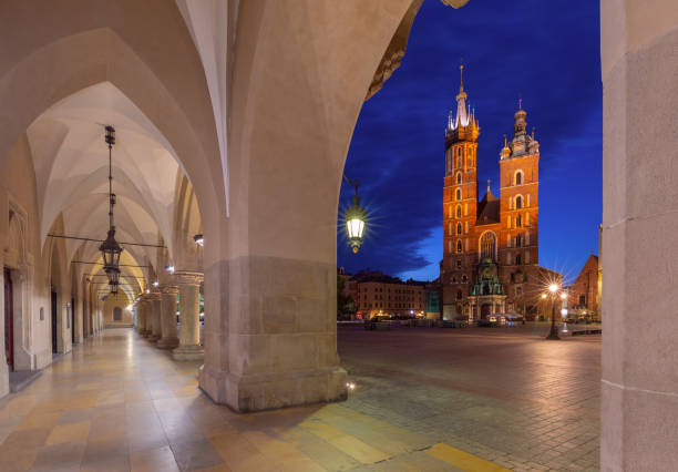 View of St. Mary's Basilica and the arches of the Cloth Hall in Krakow, Poland, during the blue hour before dawn. The illuminated basilica towers over the Main Market Square.