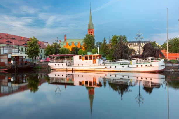 View of a church and boats reflected in the calm water of the Brda River at dawn in Bydgoszcz, Poland