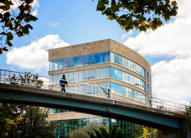 Boston,, Massachusetts, USA - October 10, 2024: Female student walking on highway overpass bridge to the Harvard Business School campus in Boston. In the background is the Tata Hall building (c. 2013) on the campus. The seven-story, glass and brick building includes residential space, classrooms, and common areas for Executive Education participants. It is named in honor of Ratan N. Tata (AMP 71, 1975). Harvard Business School (HBS) is the graduate business school of Harvard University, a private research university. It is consistently ranked among the top business schools in the world and offers a full-time MBA program, management-related doctoral programs, and executive education programs.