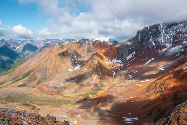 istock Top view from rocks to rounded multicolor valley with curved iron river and big sharp rocky ridge of red color. Colorful large mountain range in freshly fallen snow. Vivid high mountains in low clouds 2178273416