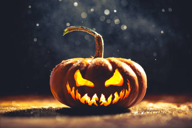 Single carved Jack o Lantern pumpkin with spooky carved face with evil grin on glittering sparkling background.
