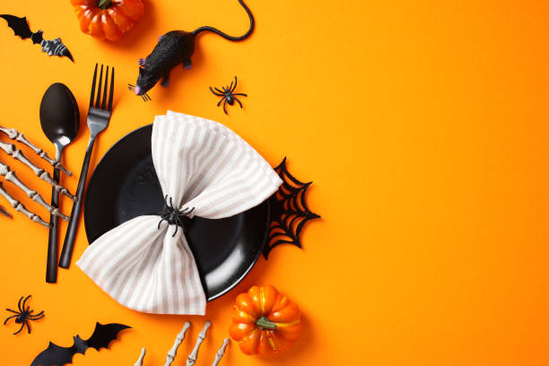 istock Halloween table setting with spooky decorations, view from above. Flat lay black plate with napkin, cutlery, bats, spiders, pumpkins, skeleton arms on orange background 2178276209