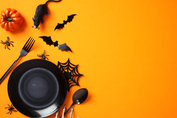 istock Halloween table setting with spooky decorations, black empty plate, cutlery, bats, spiders, pumpkins on orange background. Flat lay, top view, copy space 2178276289