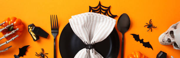 istock Halloween table setting with spooky decorations. Top view black plate with napkin, cutlery, bats, spiders, pumpkins, skull on orange background 2178276299