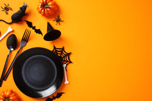 istock Halloween table setting, top view. Flat lay black empty plate, cutlery, scary decorations, bats, spiders, pumpkins on orange background. Halloween dinner concept. 2178276309