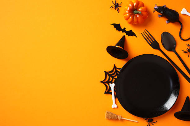 istock Halloween table setting, view from above. Flat lay black empty plate, cutlery, spooky decorations, bats, spiders, pumpkins on orange background 2178276328