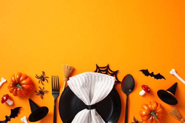 istock Halloween table setting, view from above. Flat lay composition with black plate with napkin, cutlery, spooky decorations, bats, pumpkins, skeleton arms, bones, skull on orange background 2178276354