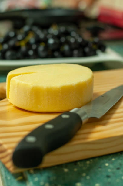 A piece of cheese with a knife and fruits in the kitchen