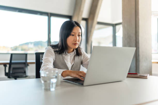 istock Asian Executive Engages with Laptop in Sunlit Office 2178280521