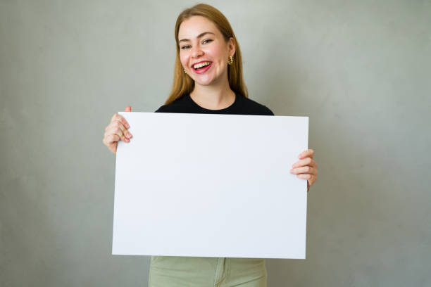 istock Smiling young woman presenting a blank white board poster for your text or image placement 2178283355
