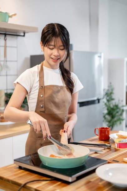 istock A beautiful, happy Asian woman frying bacons in a pan while making her breakfast in the kitchen. 2178287162
