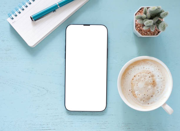 istock Blank mobile phone white screen isolated for mockup and coffee cup, cactus, pen, and notebook on blue workplace. 2178292862