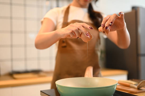istock Young woman cracking an egg into frying pan in a modern kitchen 2178295320