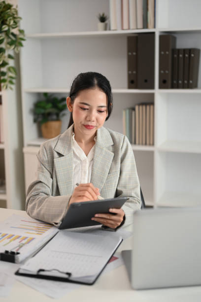 istock Attractive young businesswoman sitting at desk with documents and using a digital tablet 2178296456