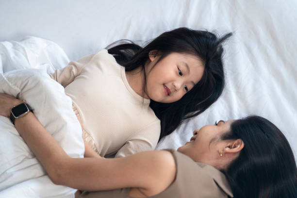 istock A joyful mother and daughter laughing together while lying on a bed. The playful moment showcases their strong bond and happiness in a comfortable home setting, surrounded by natural decor. 2178296480