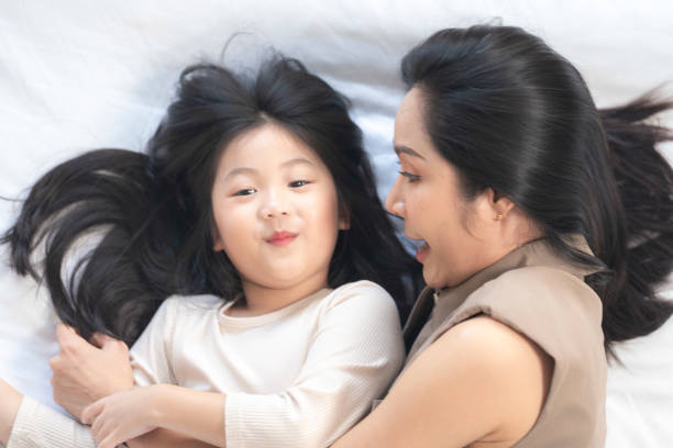 istock A joyful mother and daughter laughing together while lying on a bed. The playful moment showcases their strong bond and happiness in a comfortable home setting, surrounded by natural decor. 2178296527