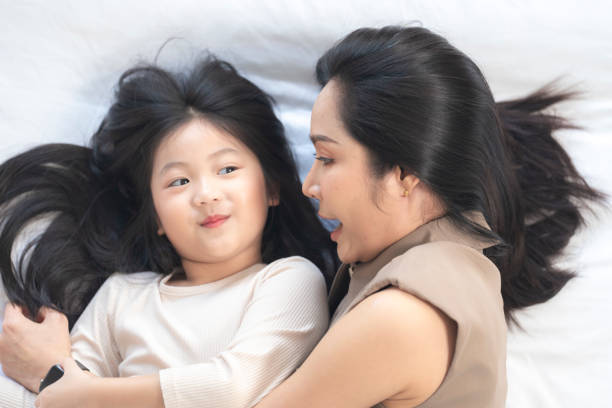 istock A joyful mother and daughter laughing together while lying on a bed. The playful moment showcases their strong bond and happiness in a comfortable home setting, surrounded by natural decor. 2178298501