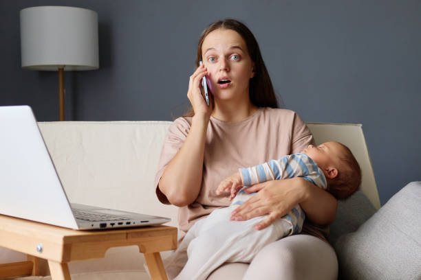 istock Shocked surprised woman working distantly during maternity leave sitting on sofa with newborn baby and talking on cell phone hearing breaking news having astonishing facial expression 2178299051