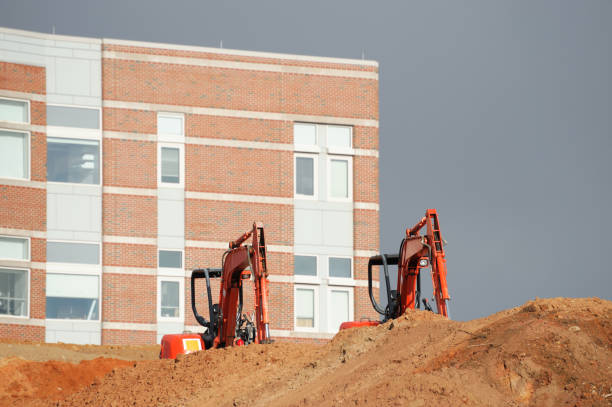 Excavators in construction site behind dirt pile in front of building