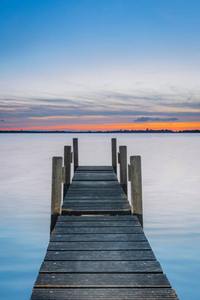 istock Sundown sky with jetty and flat horizon with trees reflecting in the tranquil lake during sunrise. 2178301198