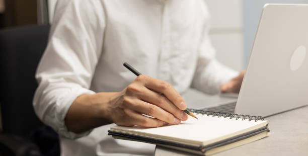 istock close up businessman hand writing content or somethings on notebook with using laptop at wooden table at home office for people and lifestyle concept 2178302292