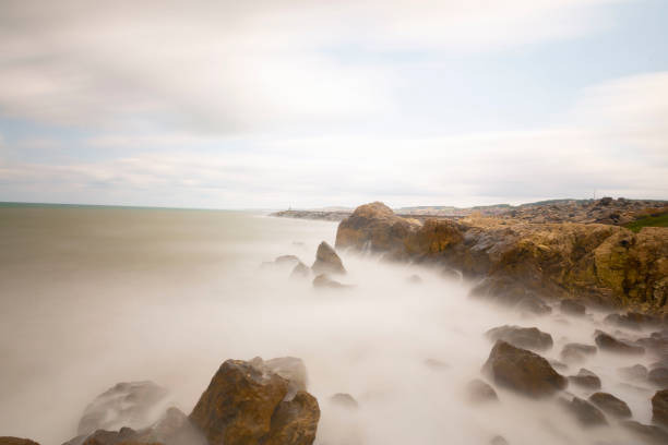 the beautiful view of a tropical beach in the morning, with white sand and coral rocks hit by ocean waves. Landscape images are taken with slow speed technique so that the splashing waves look like fog.