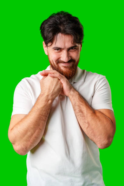 istock A man with a beard smiles mischievously while clasping his hands together against a bright green background 2178303063