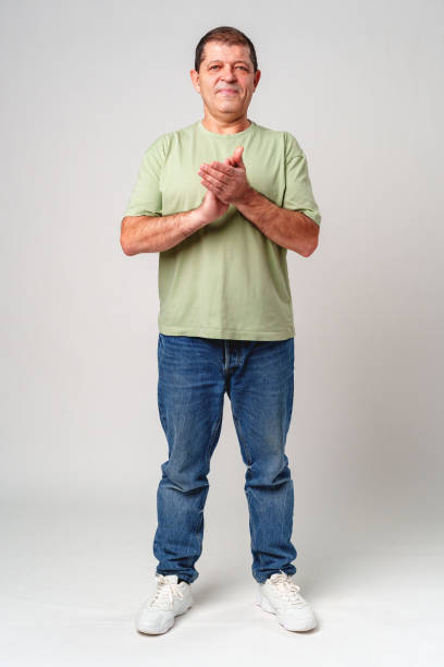 istock Elderly man claps his hands while standing against a neutral background in a casual light green shirt 2178305705