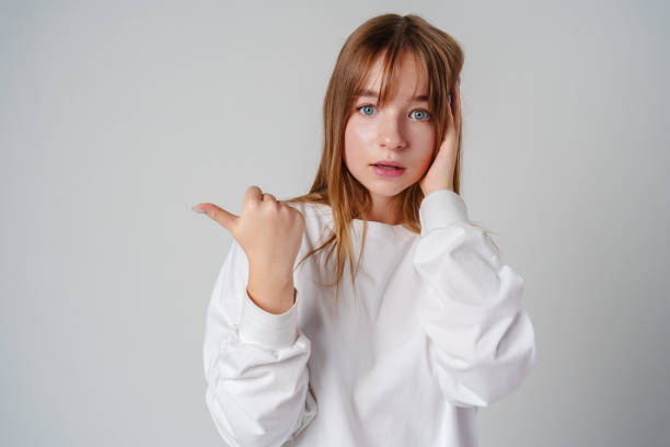 istock Young girl happily pointing against a neutral background while wearing a cozy white sweatshirt 2178305783