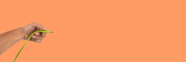 istock Black male hand holding a USB cable isolated on orange banner background 2178309188