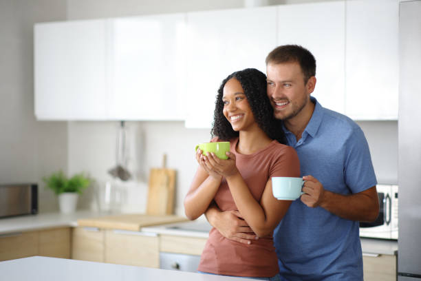 istock Happy interracial couple in the kitchen hugging and drinking 2178312230