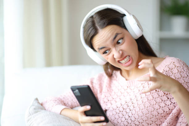 Furious woman with headphone using phone stock photo