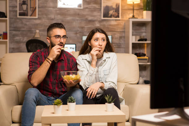 istock Couple eating chips and looking shocked at tv while watching a movie 2178313029