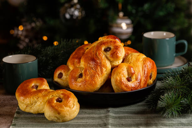 istock Christmas table with homemade  swedish St Lucia saffron buns.  Coffe or tea cups. Also called  lussekatt or lussebulle, Cornish tea treat bun or revel bun, is a spiced yeast-leavened sweet bun flavoured with saffron and contains dried  raisins. 2178314316