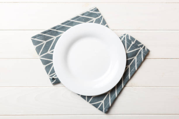 istock Top view on colored background empty round white plate on tablecloth for food. Empty dish on napkin with space for your design 2178327429