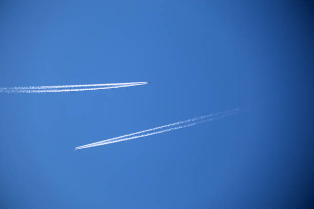 This image captures two airplanes flying high in the sky, leaving long, white contrails behind them that stretch diagonally across a deep blue sky. The planes are distant, appearing as tiny specks, but their vapor trails are prominent, slicing through the clear atmosphere with precision. The simplicity of the image, with no clouds or other visual distractions, draws attention to the movement and speed of the aircraft as they traverse the vast open sky. The contrasting white trails against the pure blue backdrop create a striking and serene visual, emphasizing the boundless freedom of flight and the vastness of the sky.