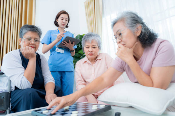 istock group of elderly women plays a board game while a healthcare professional takes notes on a tablet. The scene emphasizes senior engagement, accessibility, and supportive care in a friendly environment. 2178334830