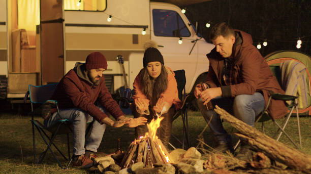istock Close friend sitting on camping chairs around camp fire 2178335933