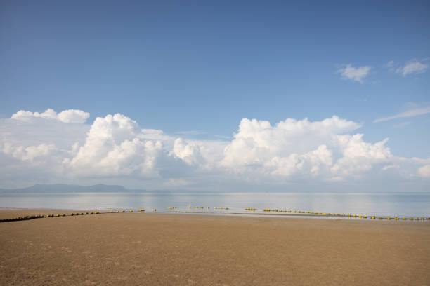 A beach with a clear blue sky and a few clouds. The sky is very bright and the clouds are scattered