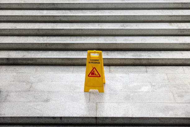 A yellow sign with a red triangle on it is on a staircase. The sign warns people to be careful on the stairs