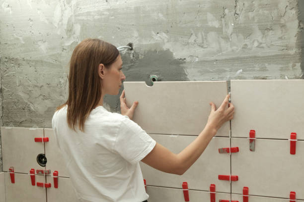istock Woman tiling bathroom walls, applying adhesive on a tile and placing ceramic tile in right position. Process of installation of tiles in the bathroom step by step. DIY home improvement. 2178340270