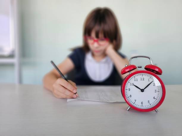 istock Schoolgirl focused on homework and alarm clock ticking 2178341317