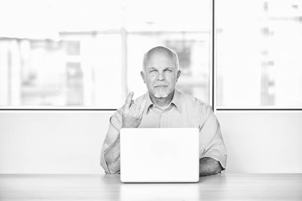 istock Senior businessman making obscene gesture at laptop in office 2178341569