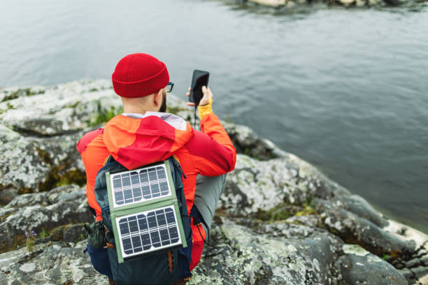 Mid adult man hiking in mountains with solar panel and charging mobile