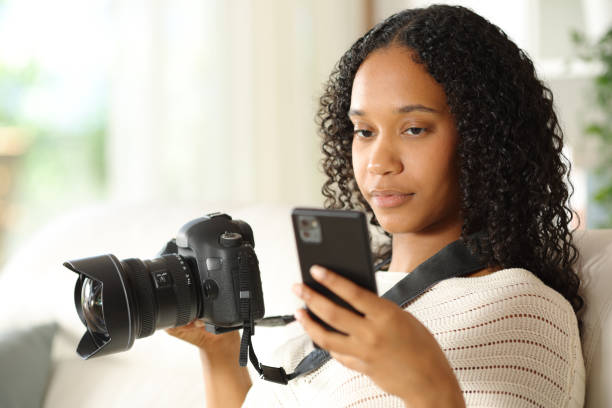 istock Black photographer at home checking phone and camera 2178342006