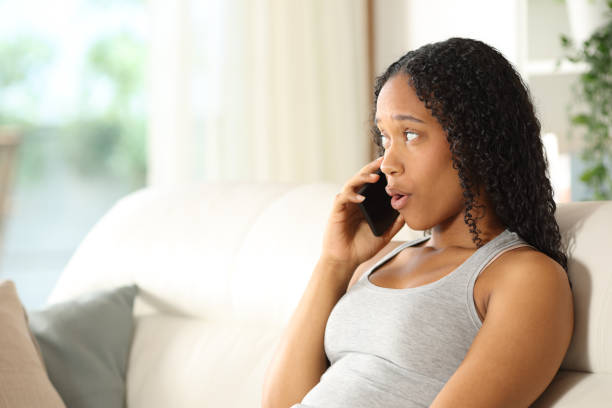 istock Surprised black woman talking on phone sitting at home 2178342055