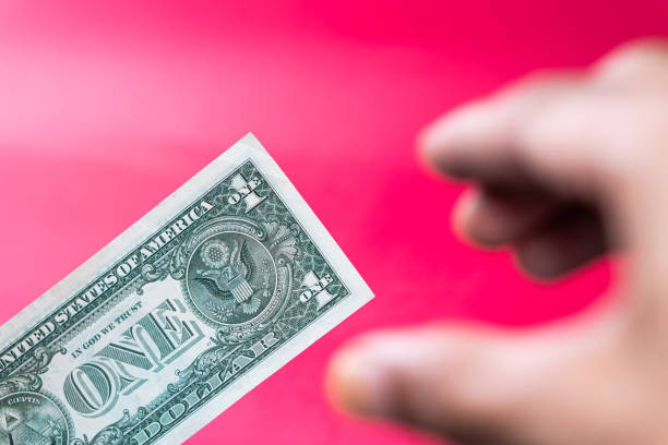 A one-dollar bill partially sticking out of a dark brown leather wallet on a red background.