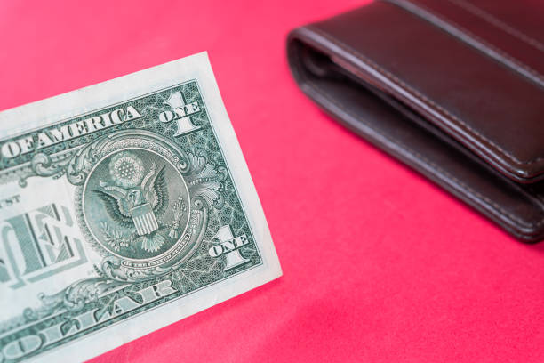 A one-dollar bill partially sticking out of a dark brown leather wallet on a red background.