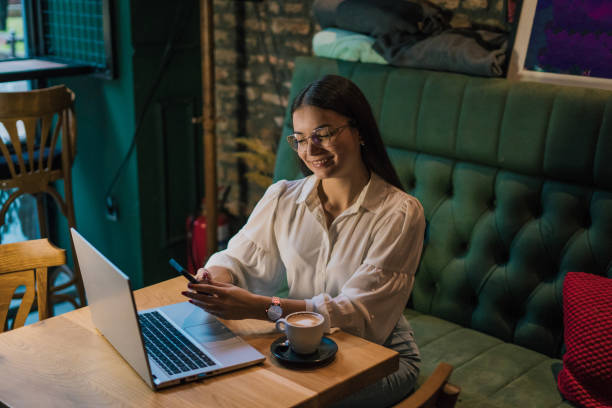 istock Young businesswoman using mobile phone while sitting at the table with laptop and working at cafe 2178344428