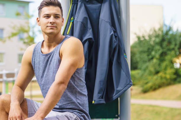 Handsome guy relaxing after outdoor workout. Fit man feeling healthy, enjoying sun. Exercising on public gym equipment in the open air.